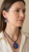 Frau trägt handgefertigtes Schmuckset Solas Autumn Blush mit Halskette und hängenden Ohrringen in Blau und Rot mit baumähnlichem abstraktem Kunstmotiv.