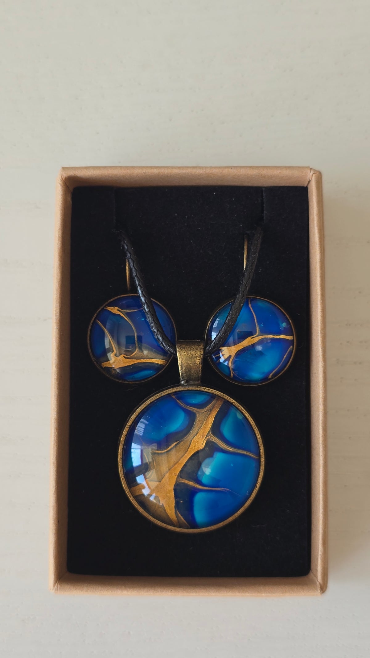 Handgefertigtes Schmuckset Solas Deep Current mit runder Halskette und passenden Ohrringen in tiefen Blau- und Goldtönen mit organischer Marmorierung.