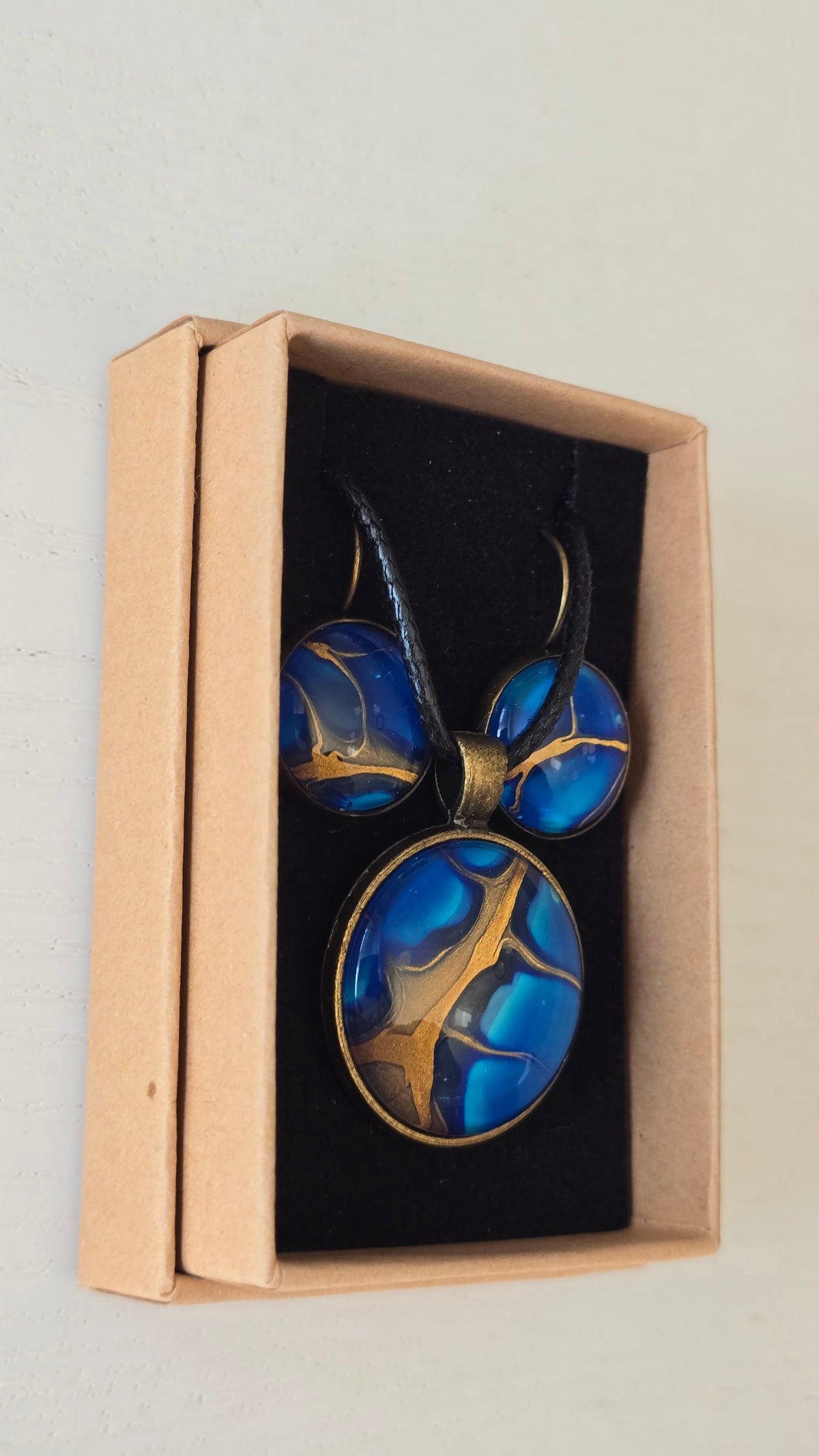 Handgefertigtes Schmuckset Solas Deep Current mit runder Halskette und passenden Ohrringen in tiefen Blau- und Goldtönen mit organischer Marmorierung.