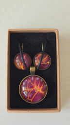 Handgefertigtes Schmuckset Solas Flare mit runder Halskette und passenden Ohrringen in Magenta-, Burgunder-, Orange- und Goldtönen mit leuchtender Marmorierung.