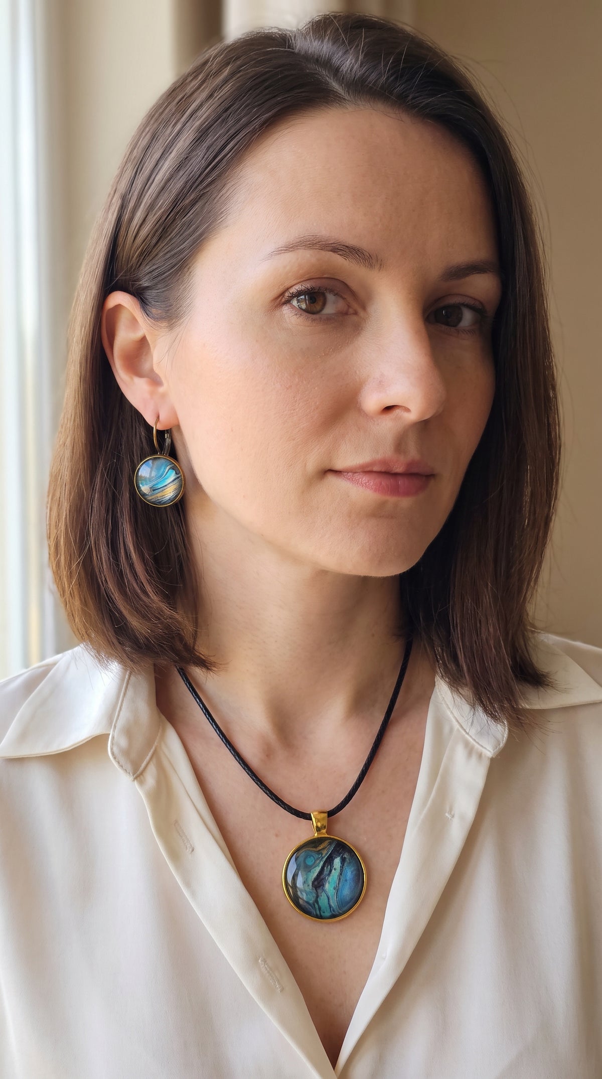 Frau trägt handgefertigtes Schmuckset Solas Golden Shore mit runder Halskette und passenden Ohrringen in Gold-, Sand-, Türkis- und Blautönen mit maritimer Marmorierung.