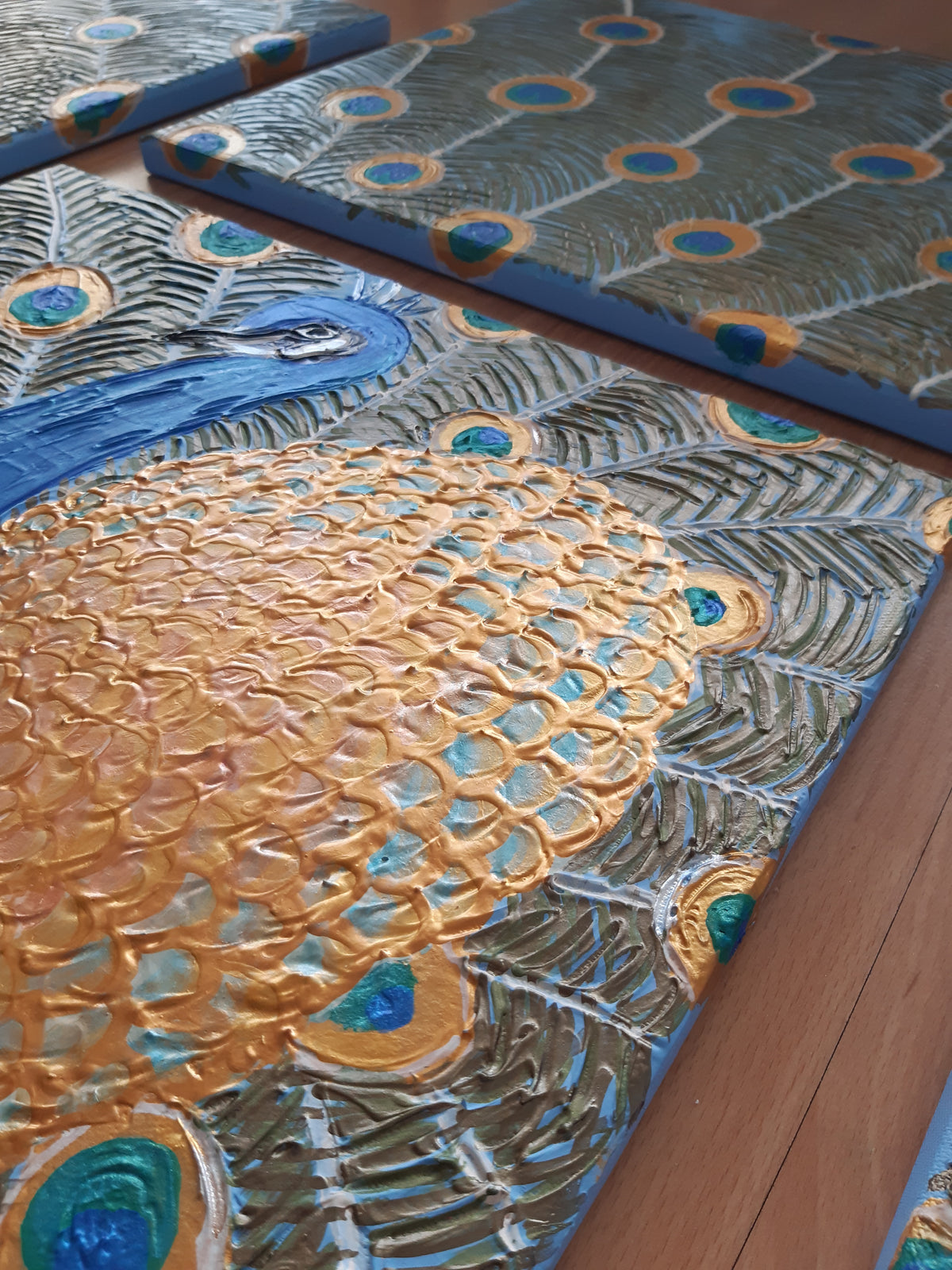 Vierteiliges handgefertigtes Leinwandbild-Set mit stilisiertem Pfauenmotiv in Blau, Türkis und Gold. Strukturierte Acrylmalerei auf Leinwand als einzigartiges Wandkunst-Unikat von Solas Artwork.