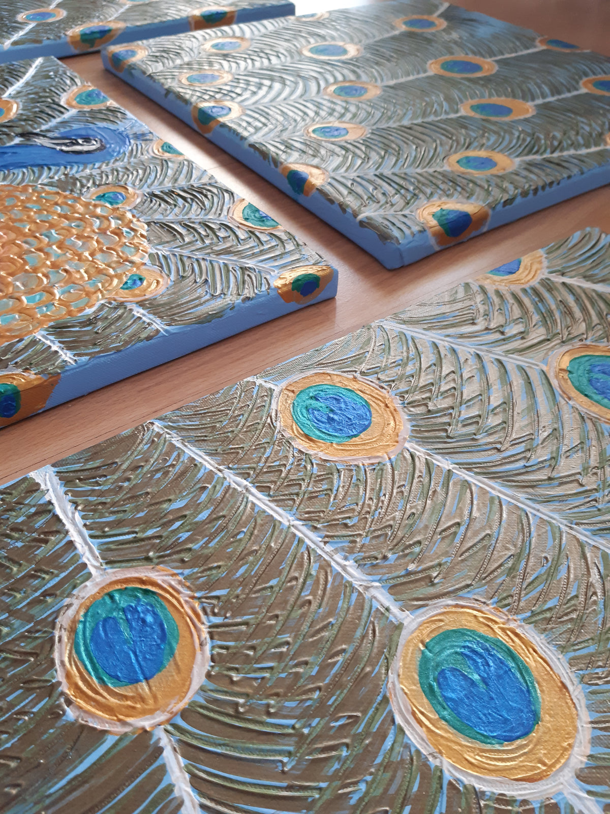 Vierteiliges handgefertigtes Leinwandbild-Set mit stilisiertem Pfauenmotiv in Blau, Türkis und Gold. Strukturierte Acrylmalerei auf Leinwand als einzigartiges Wandkunst-Unikat von Solas Artwork.