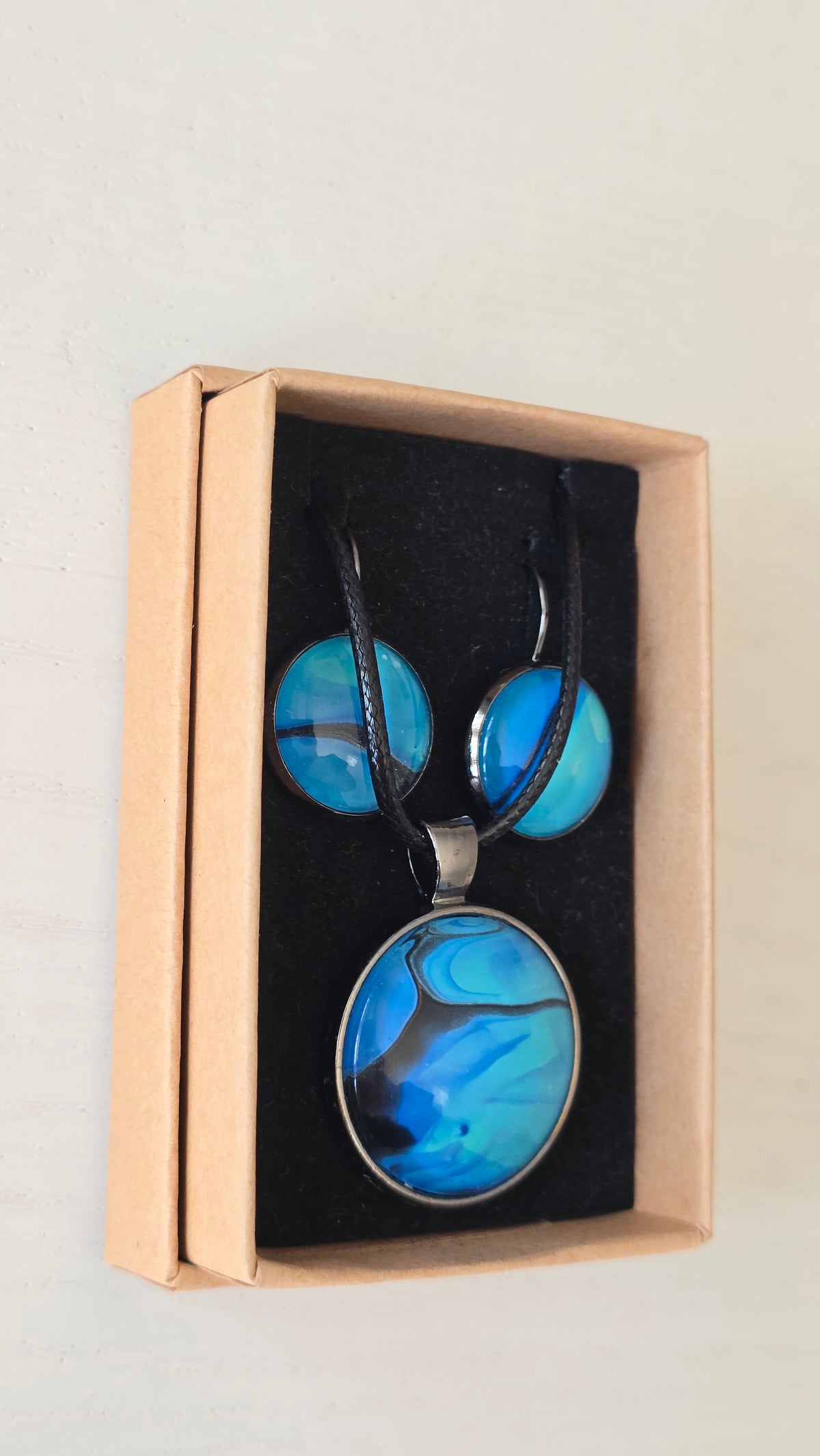 Handgefertigtes Schmuckset Solas Laguna mit rundem Anhänger und passenden Ohrringen in Blau- und Türkistönen mit fliessendem Marmormuster unter Glas.