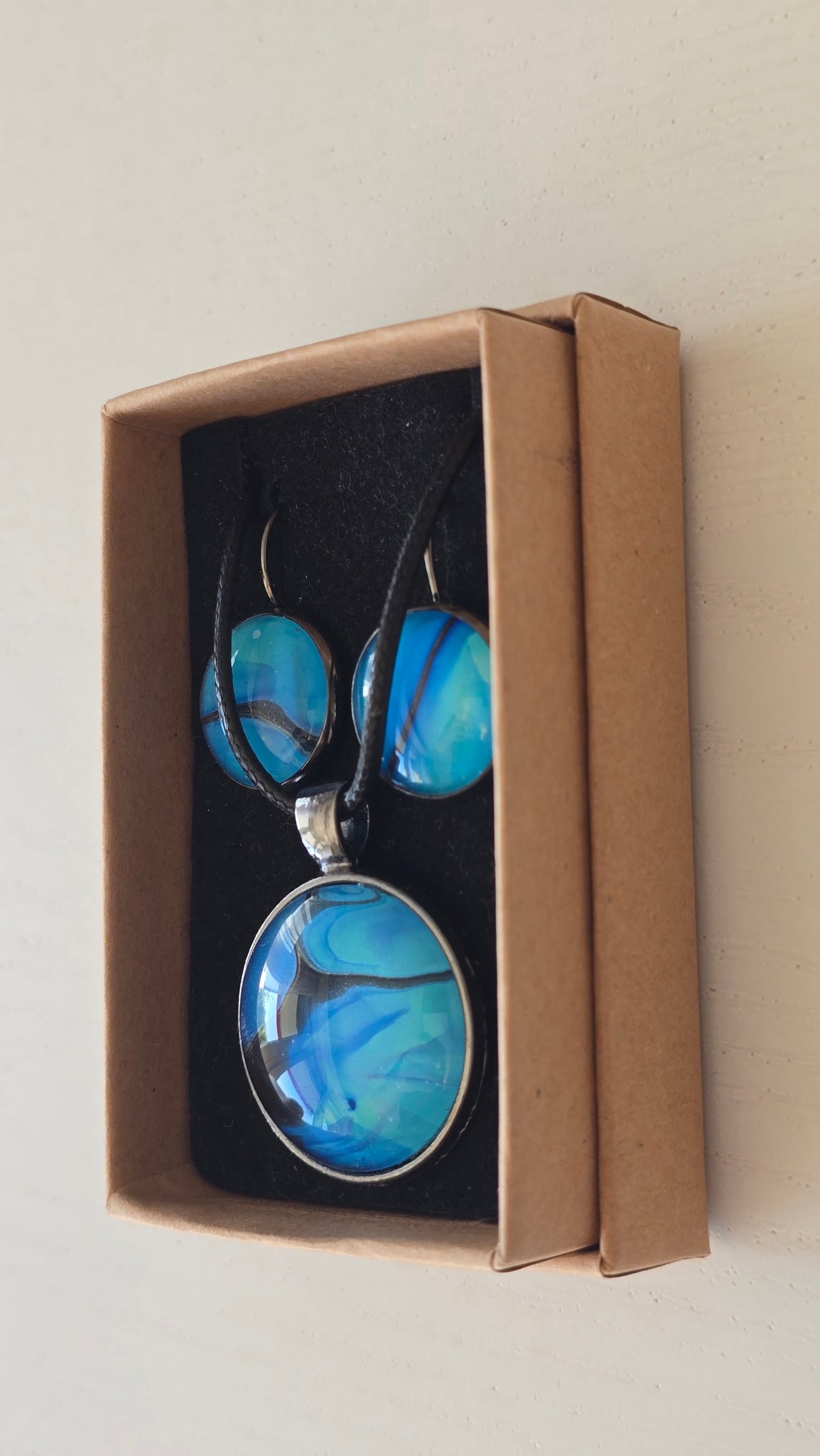 Handgefertigtes Schmuckset Solas Laguna mit rundem Anhänger und passenden Ohrringen in Blau- und Türkistönen mit fliessendem Marmormuster unter Glas.