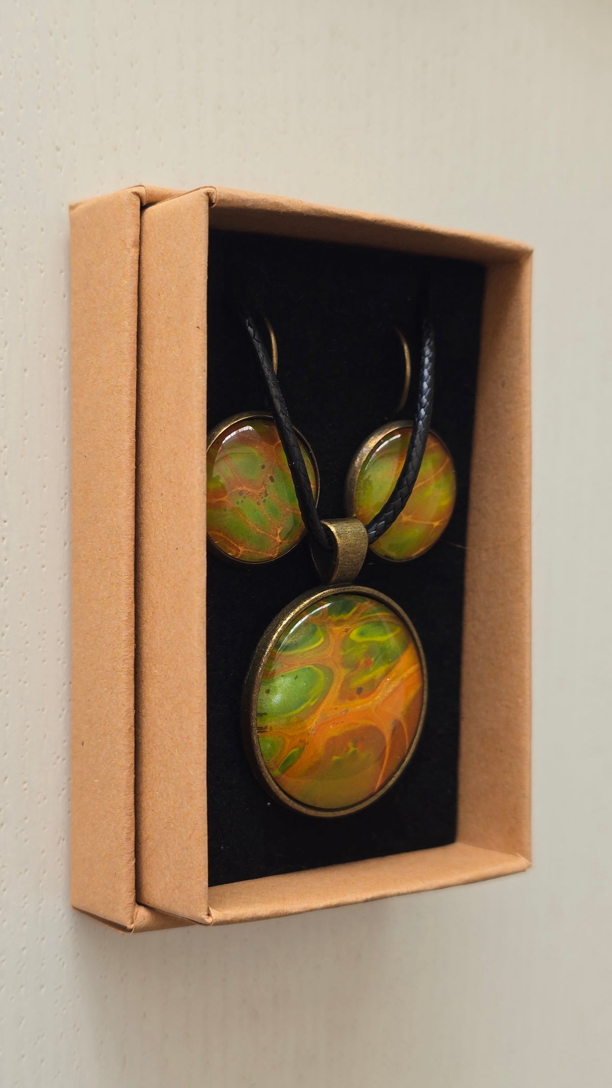 Rundes Cabochon Schmuckset mit grossem Kettenanhänger und zwei passenden Ohrringen in Grün, Orange und Gold mit fliessenden, organischen Mustern, bronzefarbenen Fassungen und schwarzem Band.