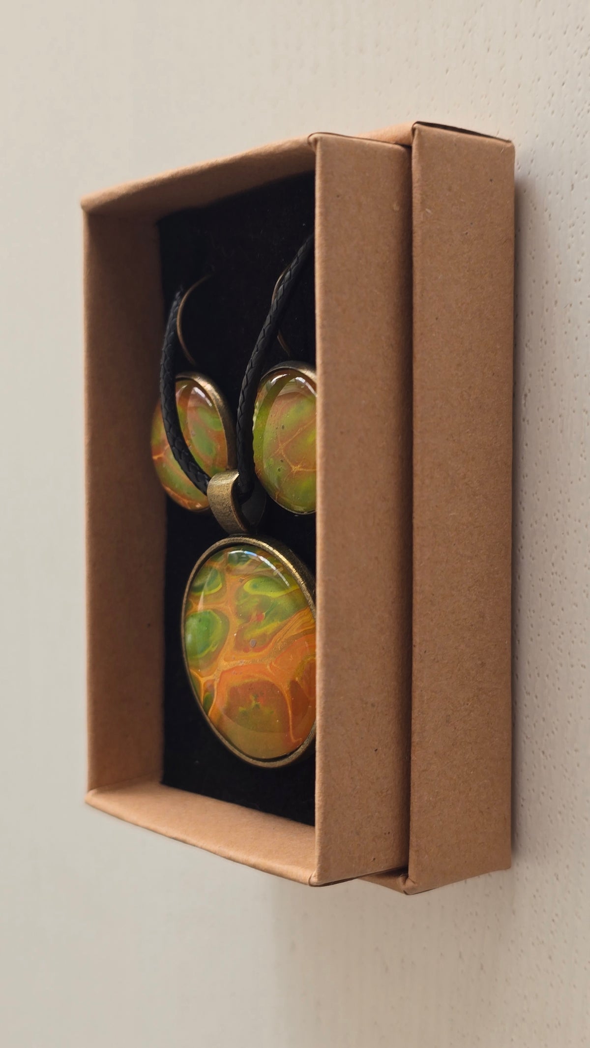 Rundes Cabochon Schmuckset mit grossem Kettenanhänger und zwei passenden Ohrringen in Grün, Orange und Gold mit fliessenden, organischen Mustern, bronzefarbenen Fassungen und schwarzem Band.