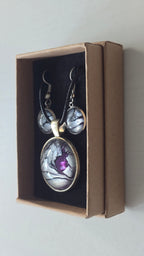 Cabochon-Schmuckset mit rundem Anhänger und zwei Ohrringen in schimmerndem Silber und Grau mit dunklen marmorierten Adern und violettem Farbkern.