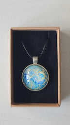 Runder Cabochon-Anhänger an schwarzem Band mit filigranem, netzartigem Muster in Aqua-, Türkis-, Hellblau- und Cremetönen.