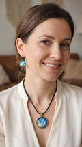 Frau trägt rundes Cabochon-Schmuckset mit grossem Halskettenanhänger und zwei passenden Ohrringen in Türkis, Blau und Creme mit feinen goldenen Akzenten.