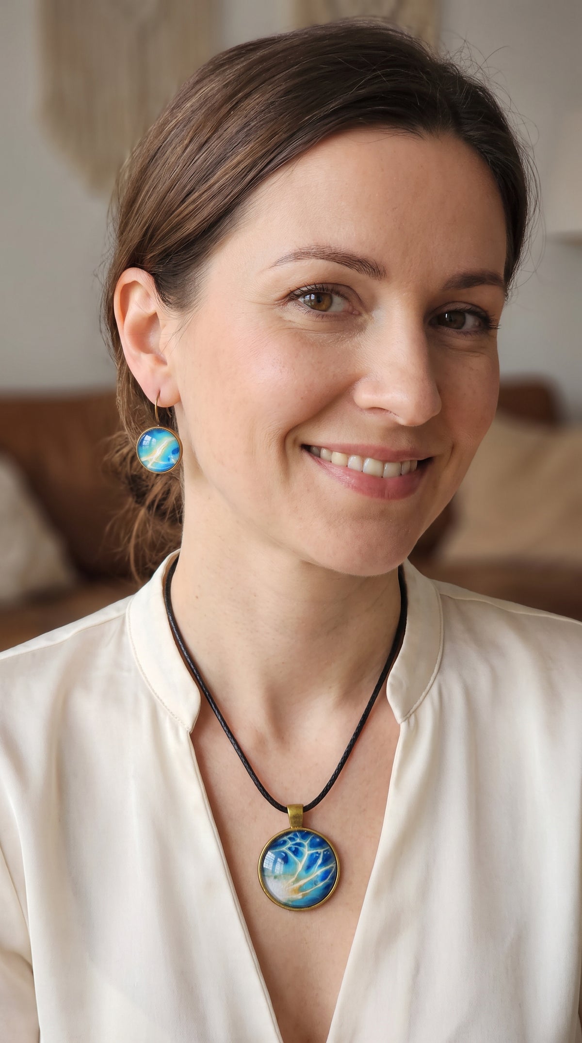Frau trägt rundes Cabochon-Schmuckset mit grossem Halskettenanhänger und zwei passenden Ohrringen in Türkis, Blau und Creme mit feinen goldenen Akzenten.