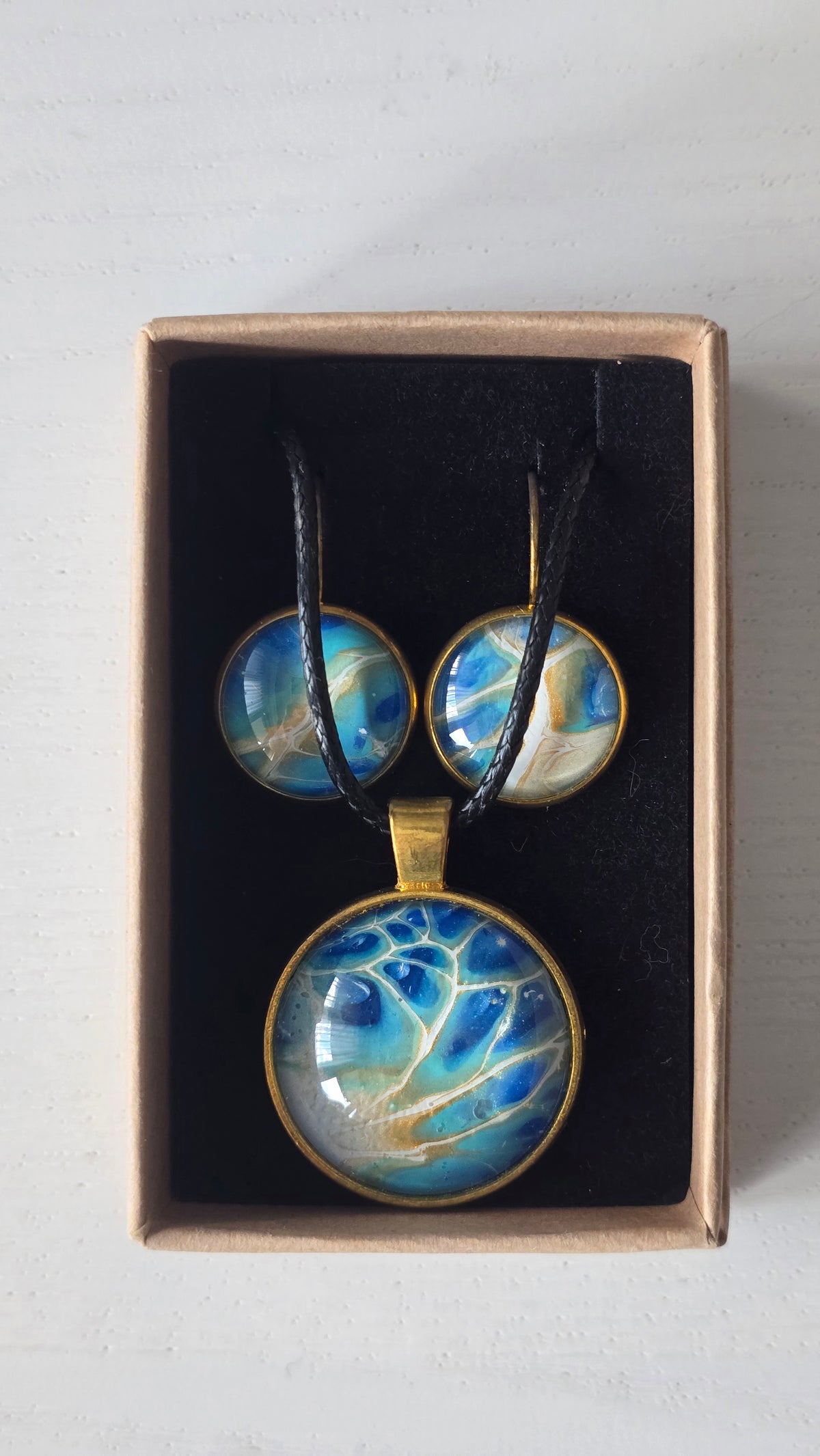 Rundes Cabochon-Schmuckset mit grossem Halskettenanhänger und zwei passenden Ohrringen in Türkis, Blau und Creme mit feinen goldenen Akzenten.