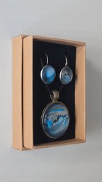 Rundes Cabochon-Schmuckset mit Anhänger und Ohrringen an schwarzem Band, mit fliessendem abstraktem Muster in Cyan, Blau, Grau und Schwarz.