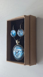 Rundes Cabochon-Schmuckset mit Anhänger und Ohrringen an schwarzem Band, mit fliessendem abstraktem Muster in Cyan, Blau, Grau und Schwarz.