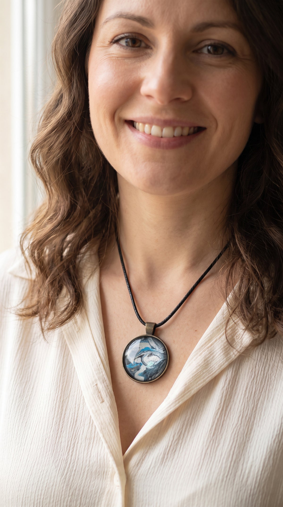 Frau trägt runde Cabochon-Kette mit fliessendem Muster in Silber, Anthrazit, Eisblau und Türkis in dunkler Metallfassung.