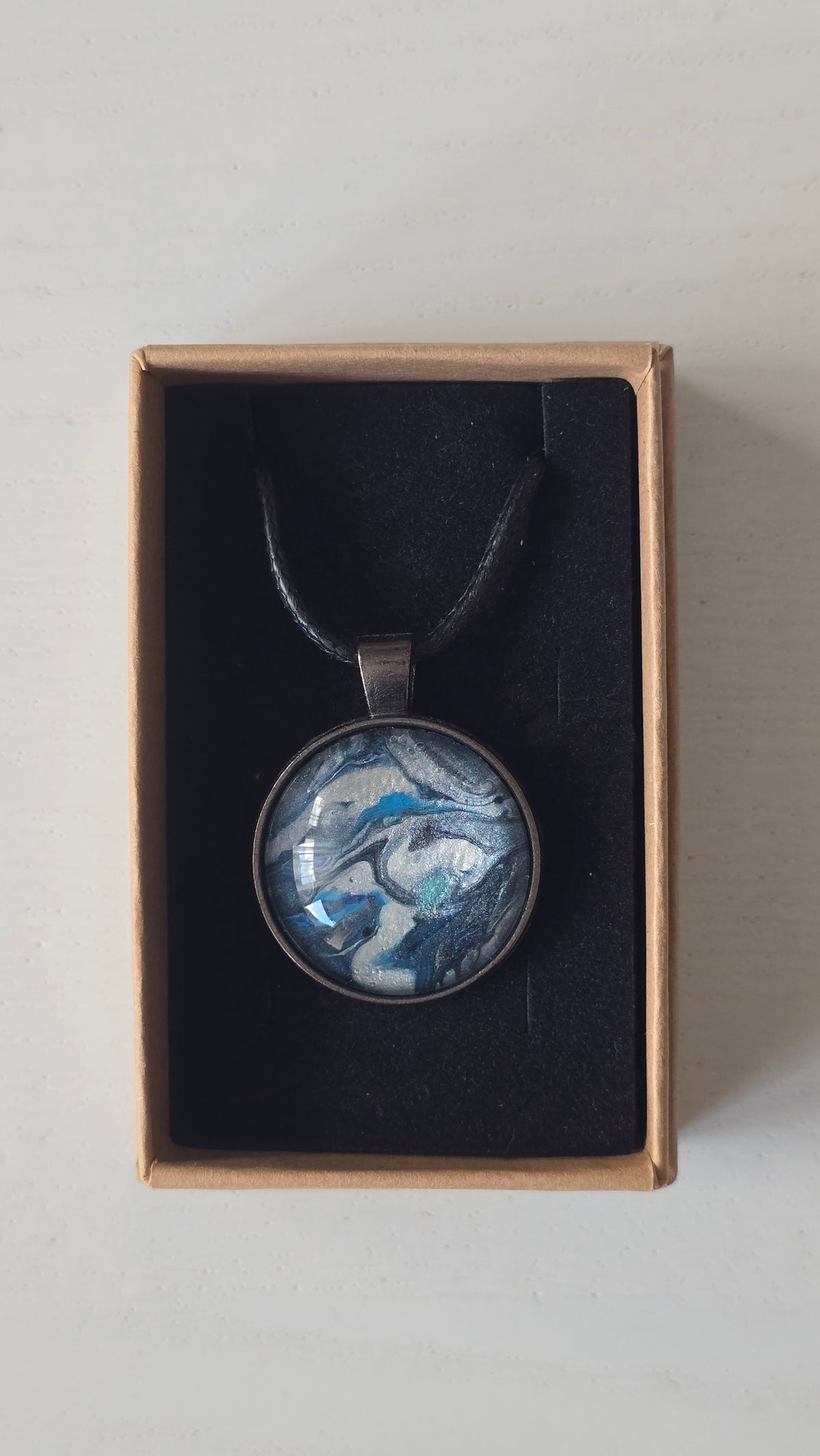 Runde Cabochon-Kette mit fliessendem Muster in Silber, Anthrazit, Eisblau und Türkis in dunkler Metallfassung.