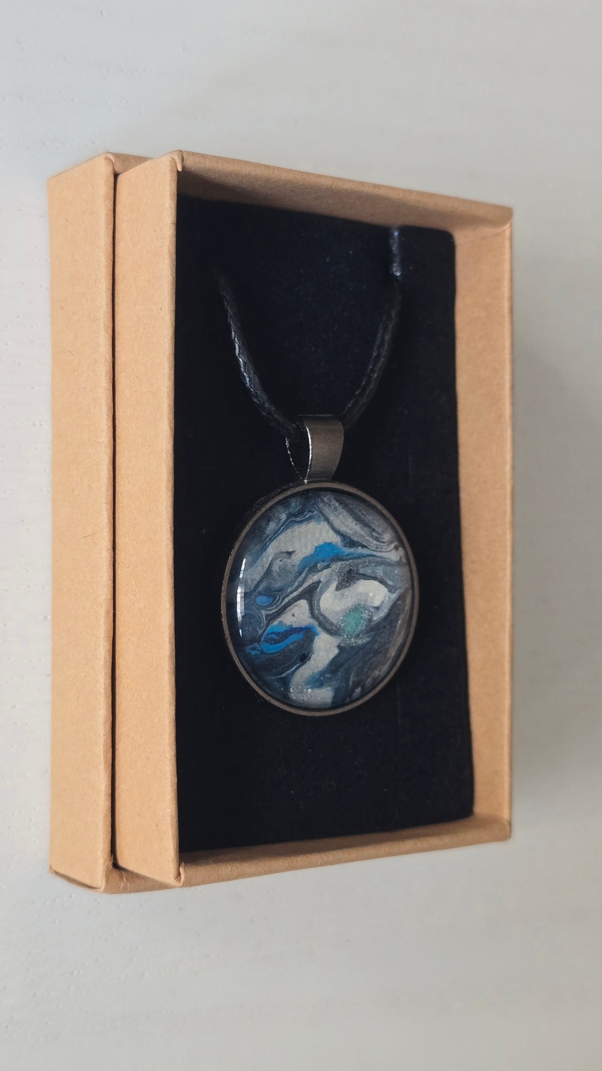 Runde Cabochon-Kette mit fliessendem Muster in Silber, Anthrazit, Eisblau und Türkis in dunkler Metallfassung.