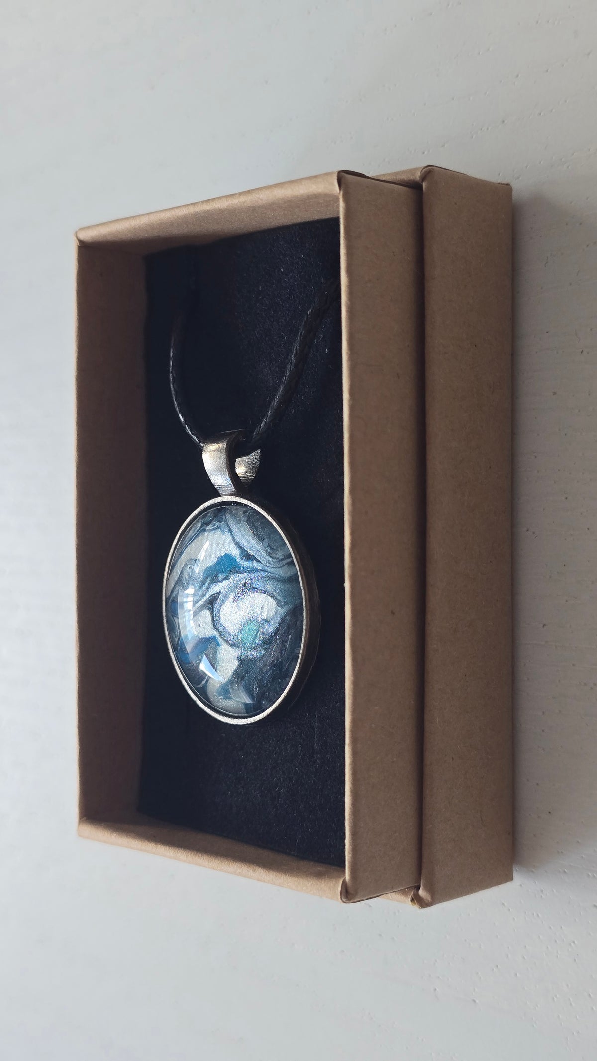 Runde Cabochon-Kette mit fliessendem Muster in Silber, Anthrazit, Eisblau und Türkis in dunkler Metallfassung.