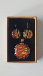 Cabochon-Schmuckset mit rundem Anhänger und zwei Ohrringen mit organischem Muster in Rostrot, Orange und leuchtendem Grün, kupferfarbenen Fassungen und schwarzem Textilband.