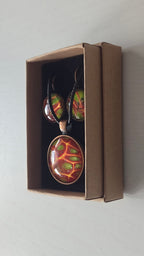 Cabochon-Schmuckset mit rundem Anhänger und zwei Ohrringen mit organischem Muster in Rostrot, Orange und leuchtendem Grün, kupferfarbenen Fassungen und schwarzem Textilband.