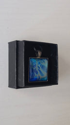 Quadratischer Cabochon-Anhänger an schwarzem Band mit abstraktem, fliessendem Muster in intensiven Blau-, Türkis- und hell schimmernden Nuancen.