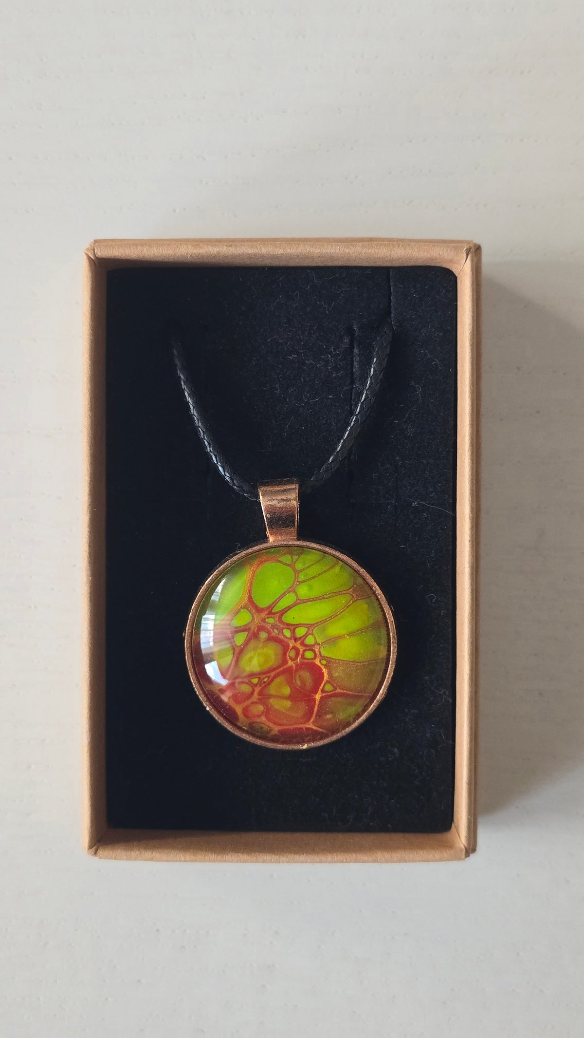 Runde Cabochon Kette Solas Bloom Temper mit leuchtend grüner, kupferroter Farbstruktur, bronzefarbener Fassung und schwarzem Band.
