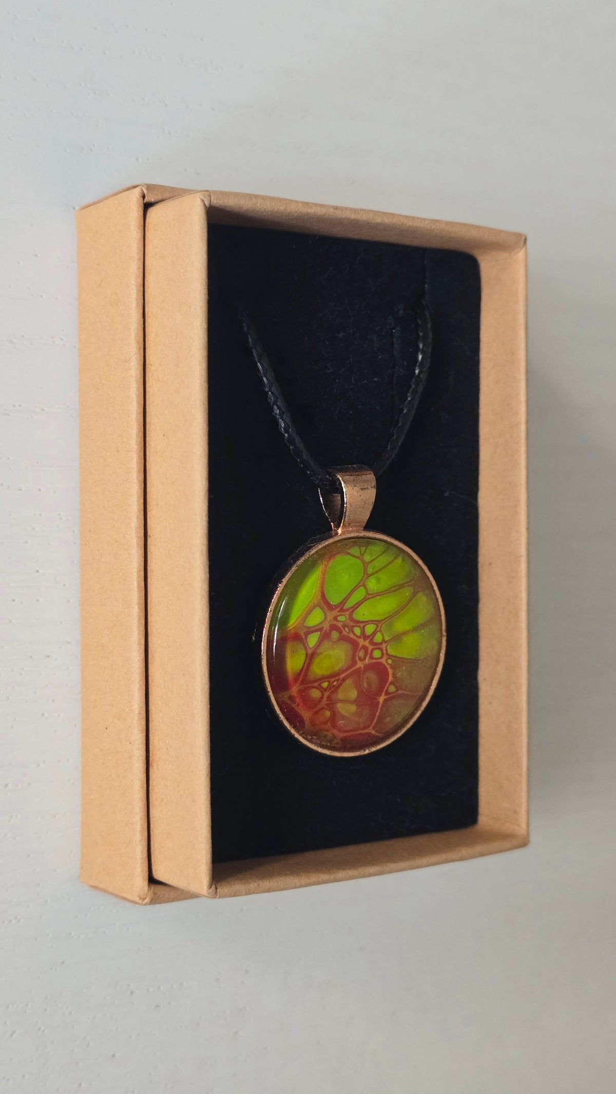 Runde Cabochon Kette Solas Bloom Temper mit leuchtend grüner, kupferroter Farbstruktur, bronzefarbener Fassung und schwarzem Band.
