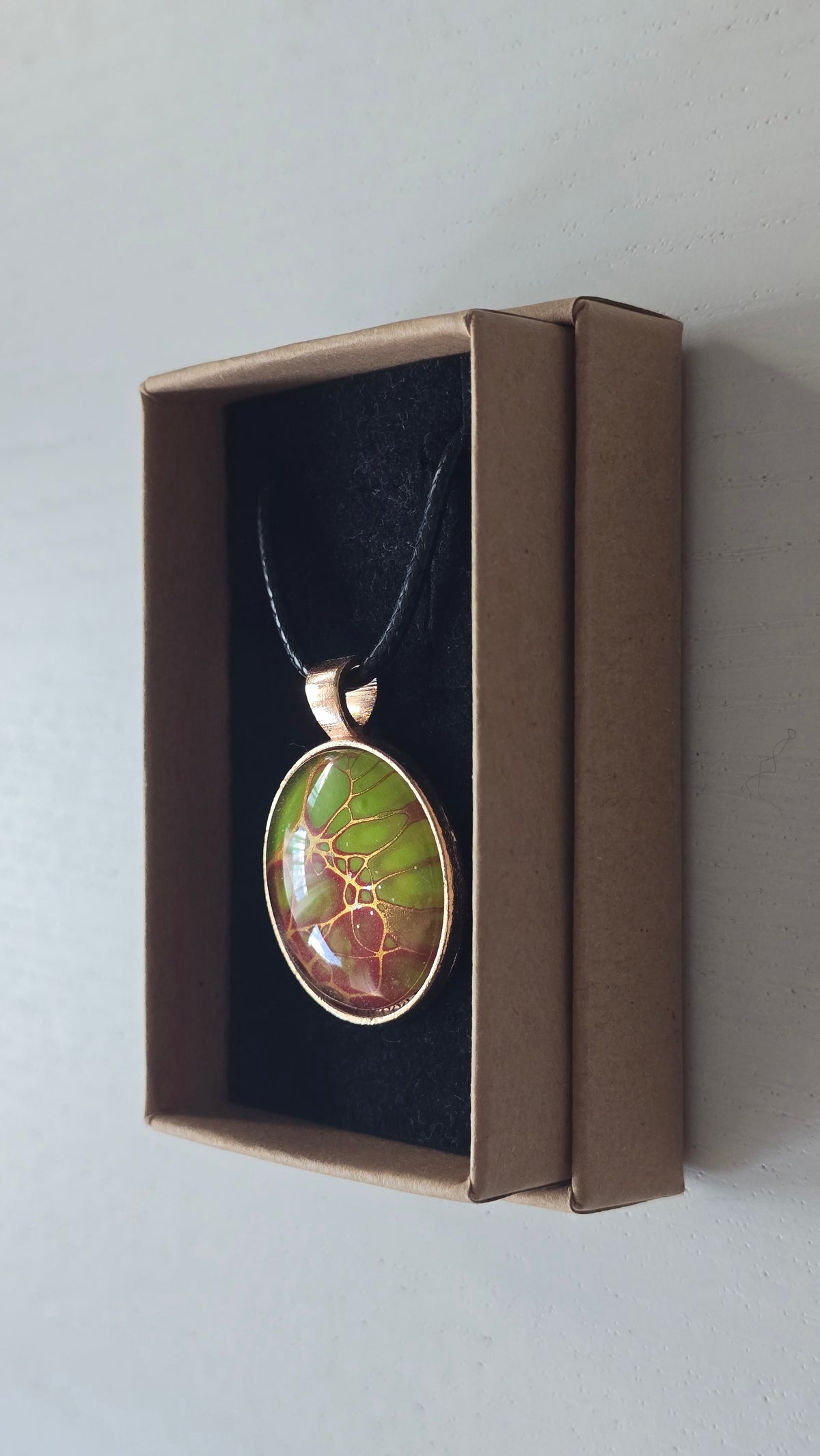 Runde Cabochon Kette Solas Bloom Temper mit leuchtend grüner, kupferroter Farbstruktur, bronzefarbener Fassung und schwarzem Band.