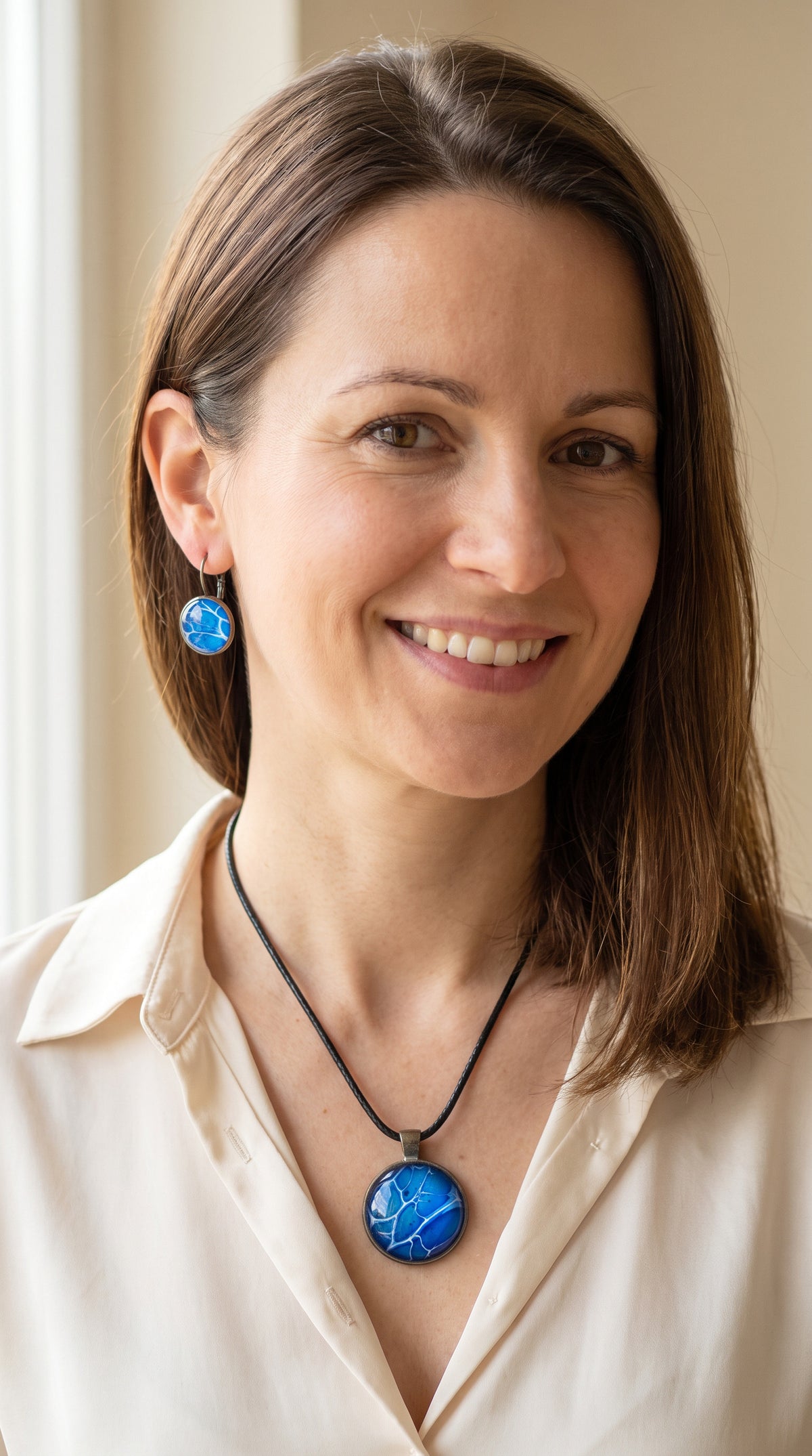 Frau trägt rundes Cabochon-Schmuckset mit Anhänger und Ohrringen an schwarzem Band, in leuchtendem Blau und Cyan mit feinen weissen, verzweigten Linien.