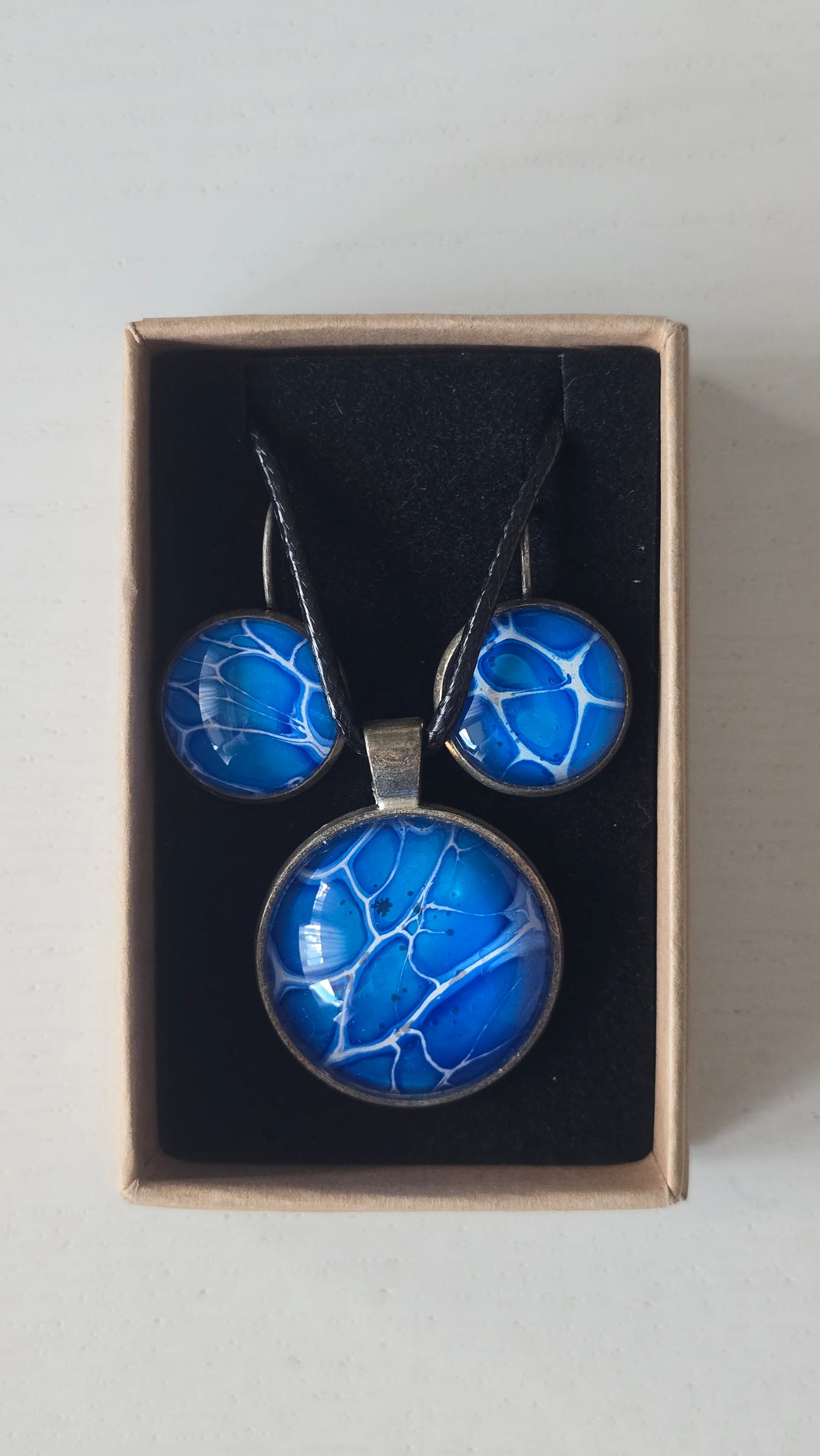 Rundes Cabochon-Schmuckset mit Anhänger und Ohrringen an schwarzem Band, in leuchtendem Blau und Cyan mit feinen weissen, verzweigten Linien.