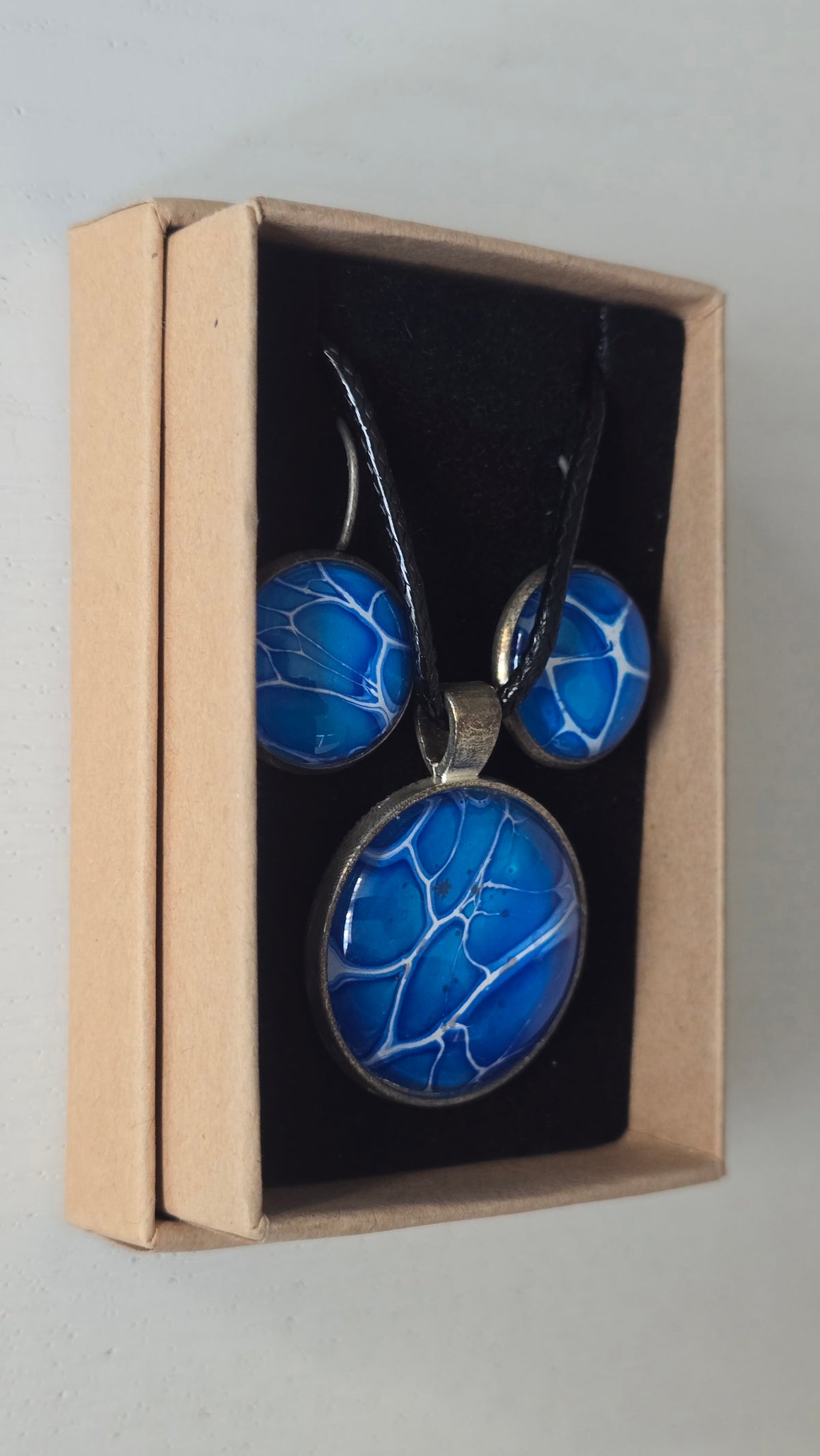 Rundes Cabochon-Schmuckset mit Anhänger und Ohrringen an schwarzem Band, in leuchtendem Blau und Cyan mit feinen weissen, verzweigten Linien.