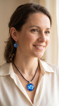 Frau trägt cabochon Schmuckset Solas Blue Fusion mit runder Kette und zwei Ohrringen in Dunkelblau, Kobaltblau, Türkis und Weiss, silberfarbenen Fassungen und schwarzem Band.