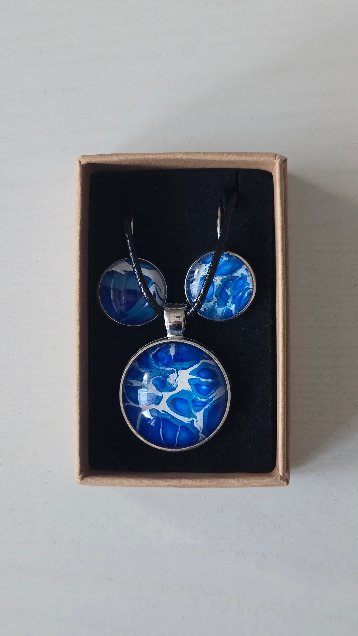 Cabochon Schmuckset Solas Blue Fusion mit runder Kette und zwei Ohrringen in Dunkelblau, Kobaltblau, Türkis und Weiss, silberfarbenen Fassungen und schwarzem Band.