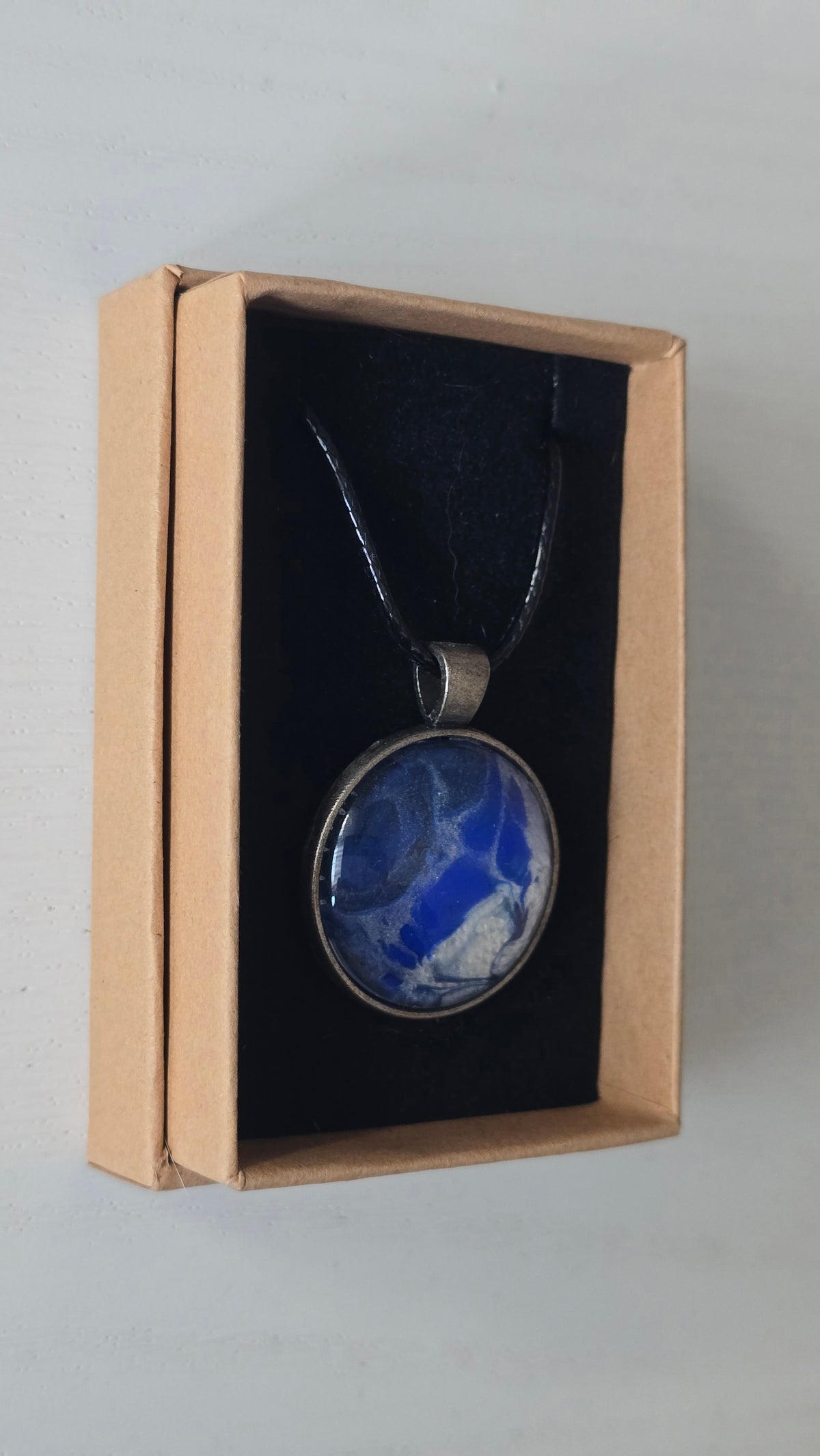 Runde Cabochon Kette Solas Blue Glacier in Kobaltblau, Silber und Weiss mit dunkler Metallfassung und schwarzem Band.