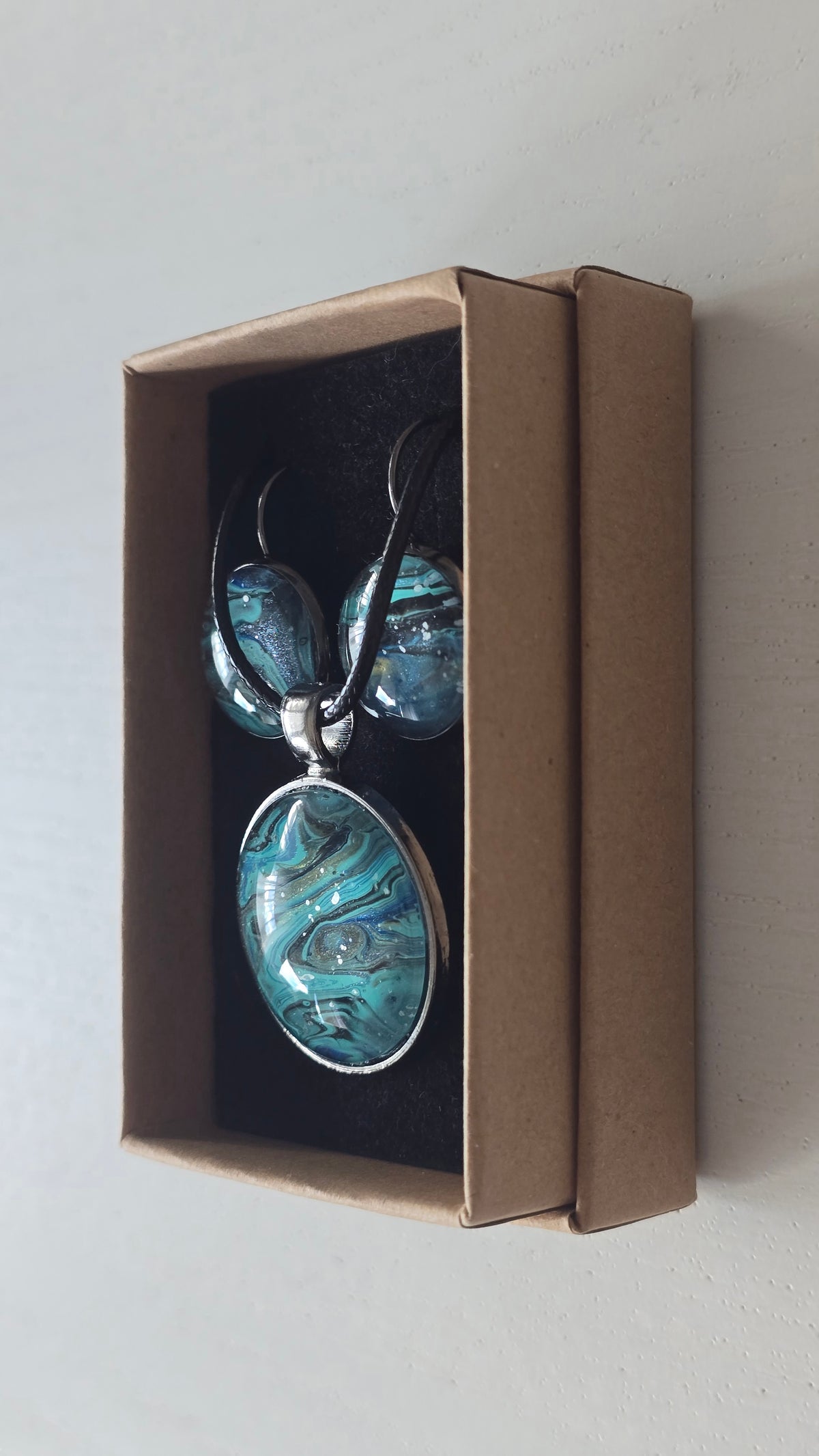 Rundes Cabochon-Schmuckset mit Halskettenanhänger und passenden Ohrringen in Türkis, Blau, Schwarz und Grau mit fliessender marmorierter Maserung.
