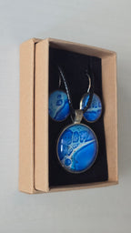 Rundes Cabochon-Schmuckset mit Anhänger und Ohrringen an schwarzem Band, in Kobaltblau, Cyan und Türkis mit runden Zellformen und dunkelblauen Konturen.