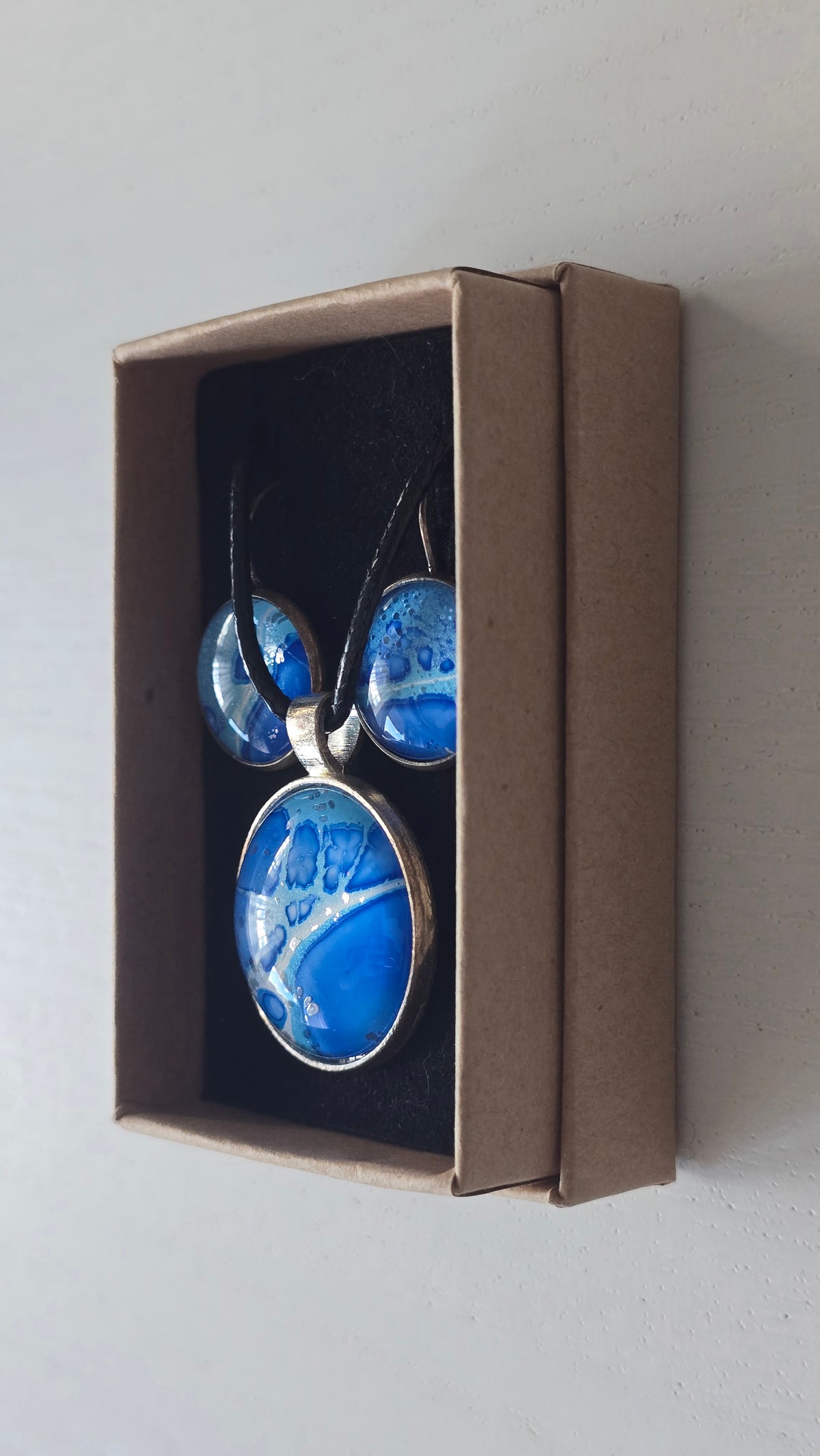 Rundes Cabochon-Schmuckset mit Anhänger und Ohrringen an schwarzem Band, in Kobaltblau, Cyan und Türkis mit runden Zellformen und dunkelblauen Konturen.