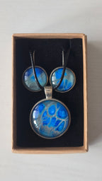 Rundes Cabochon-Schmuckset mit grossem Halskettenanhänger und zwei passenden Ohrringen in leuchtendem Blau auf silbrig-türkisem Grund.