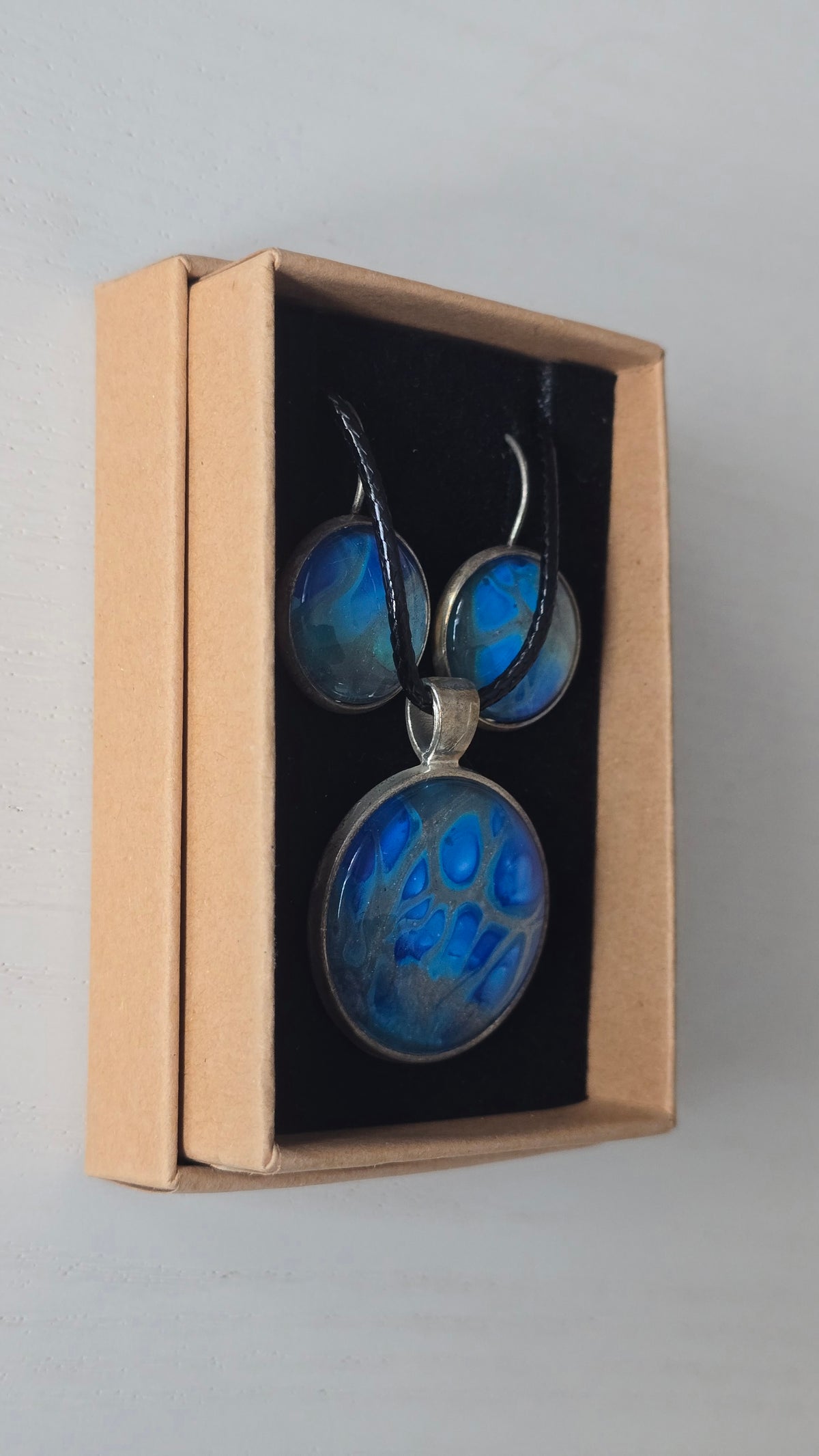 Rundes Cabochon-Schmuckset mit grossem Halskettenanhänger und zwei passenden Ohrringen in leuchtendem Blau auf silbrig-türkisem Grund.