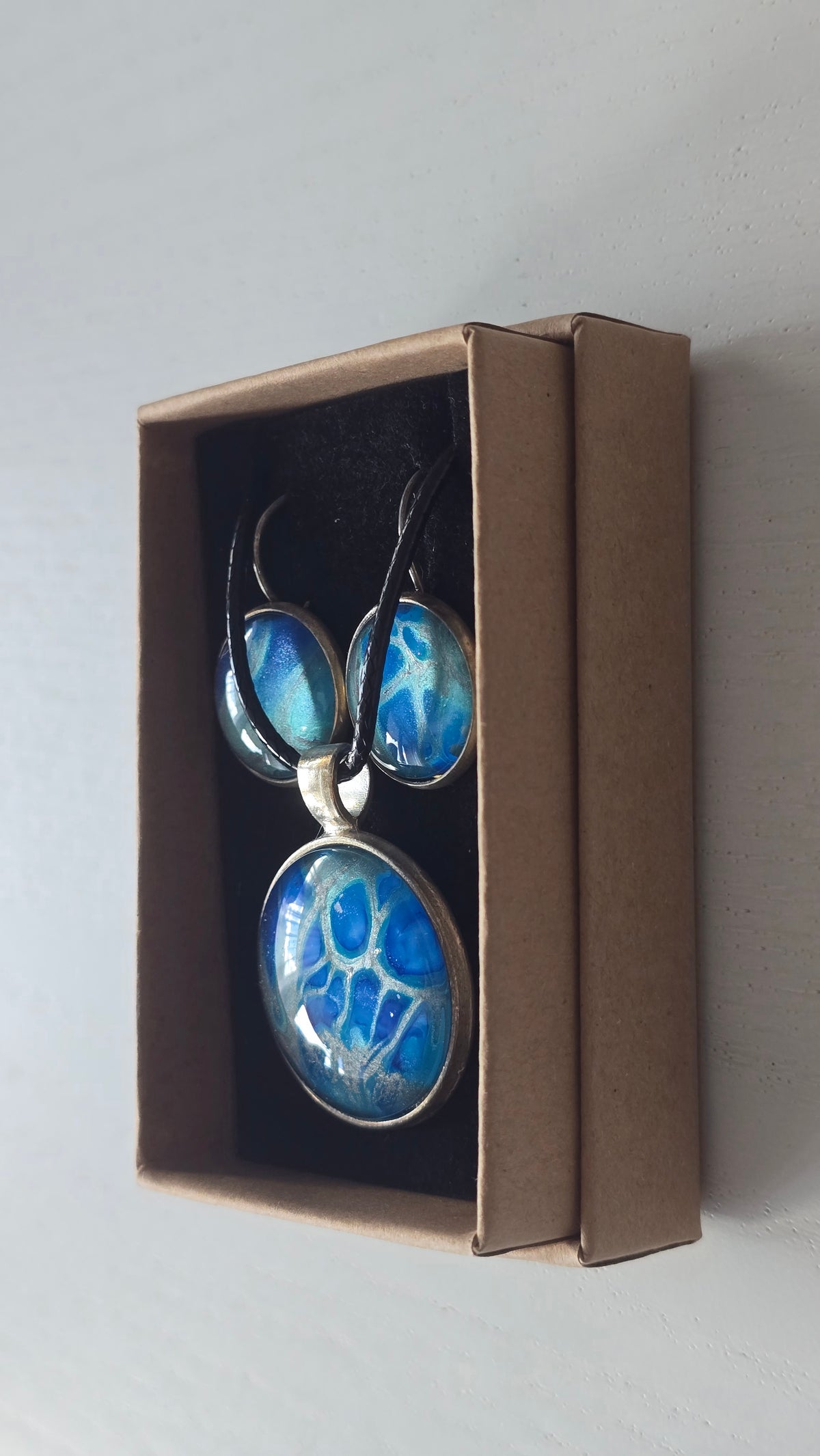 Rundes Cabochon-Schmuckset mit grossem Halskettenanhänger und zwei passenden Ohrringen in leuchtendem Blau auf silbrig-türkisem Grund.