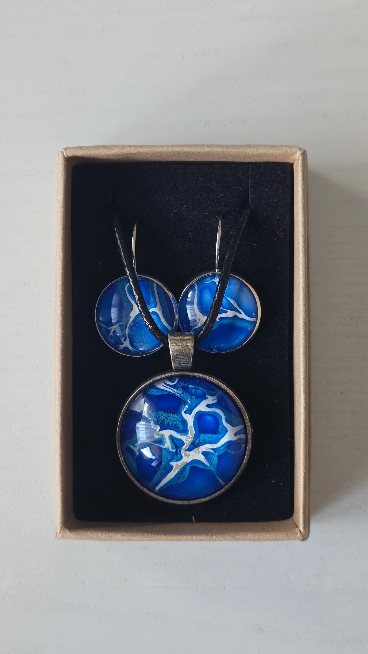 Rundes Cabochon Schmuckset mit grossem Kettenanhänger und zwei passenden Ohrringen in kräftigem Blau und Türkis mit weissen, verzweigten Strukturen, silberfarbenen Fassungen und schwarzem Band.