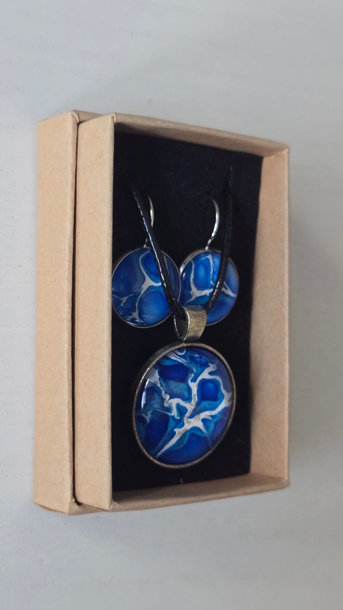 Rundes Cabochon Schmuckset mit grossem Kettenanhänger und zwei passenden Ohrringen in kräftigem Blau und Türkis mit weissen, verzweigten Strukturen, silberfarbenen Fassungen und schwarzem Band.