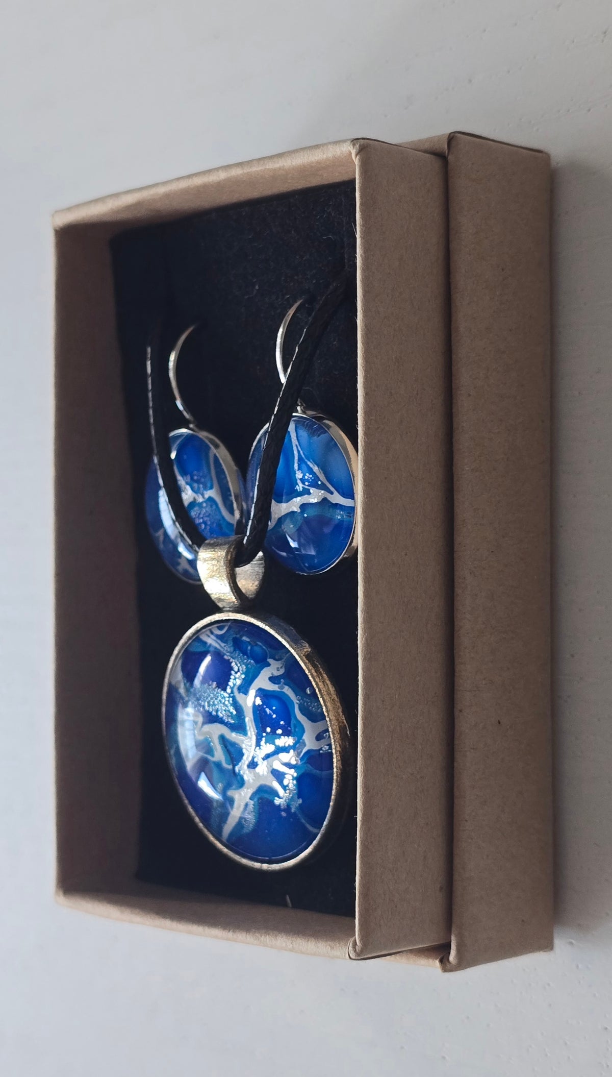 Rundes Cabochon Schmuckset mit grossem Kettenanhänger und zwei passenden Ohrringen in kräftigem Blau und Türkis mit weissen, verzweigten Strukturen, silberfarbenen Fassungen und schwarzem Band.