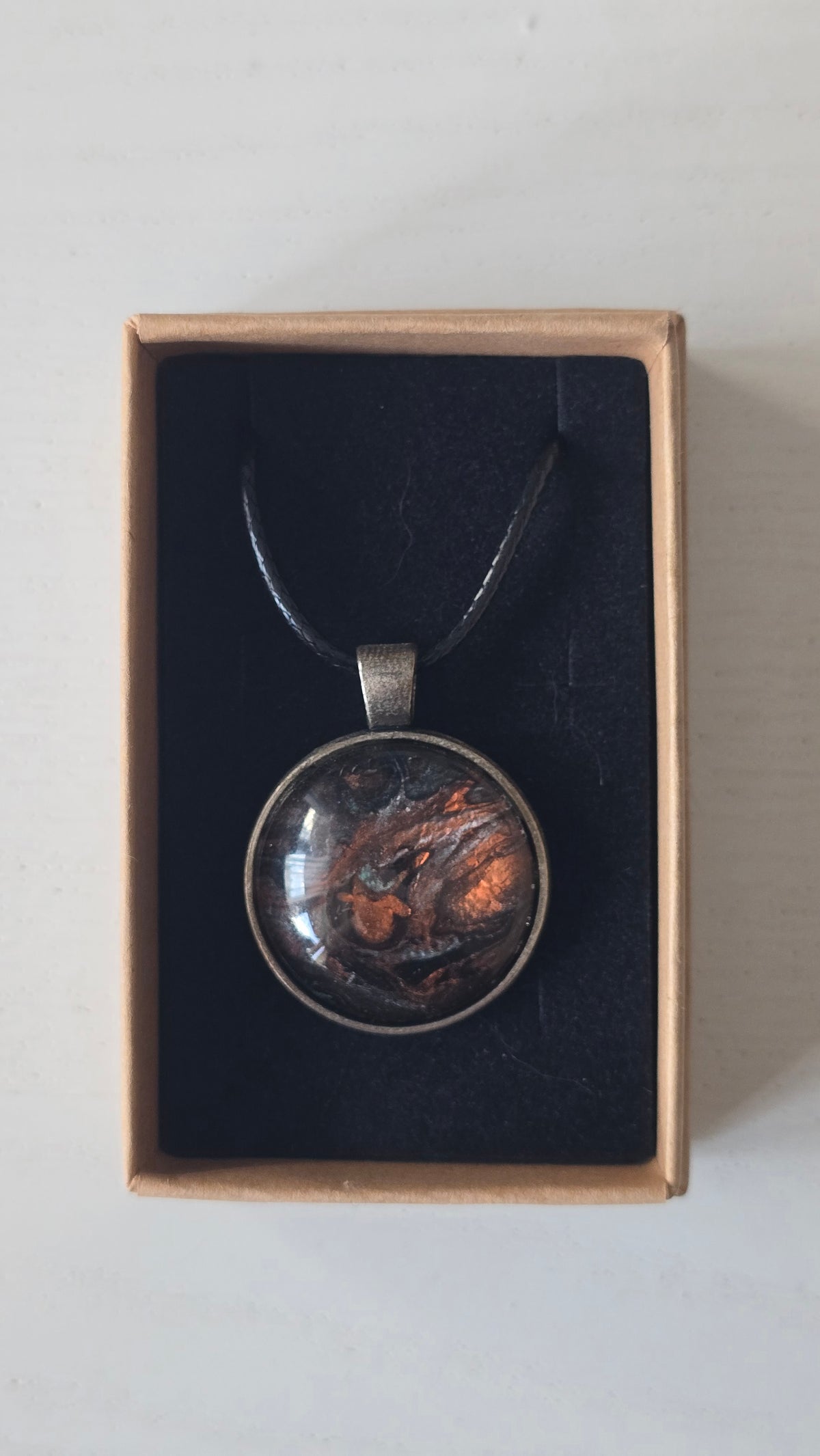 Runde Cabochon Kette Solas Burnt Earth in Kupfer, Bronze und Schwarz mit dunkler Metallfassung und schwarzem Band.