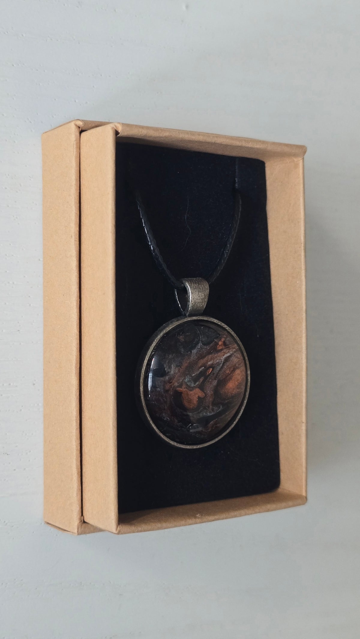 Runde Cabochon Kette Solas Burnt Earth in Kupfer, Bronze und Schwarz mit dunkler Metallfassung und schwarzem Band.