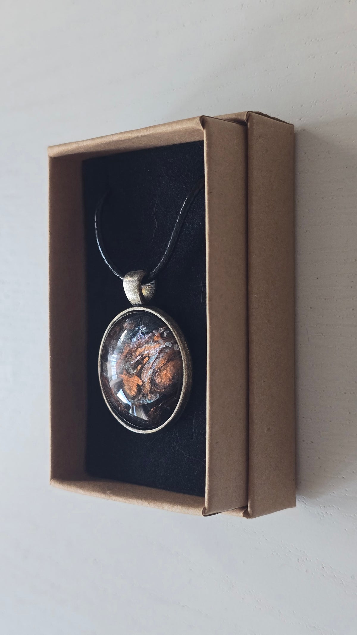 Runde Cabochon Kette Solas Burnt Earth in Kupfer, Bronze und Schwarz mit dunkler Metallfassung und schwarzem Band.