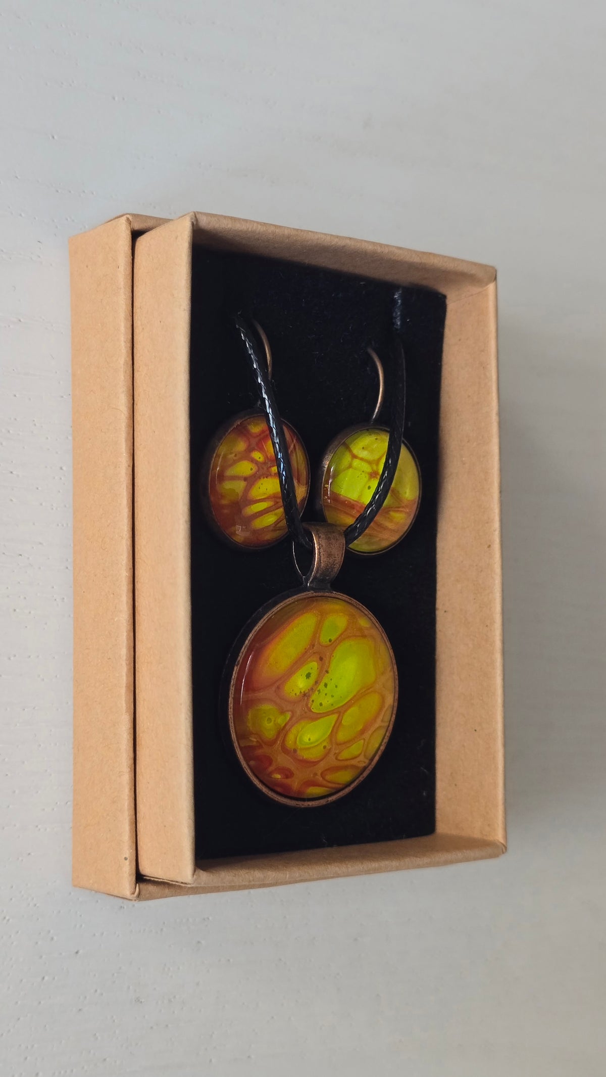 Rundes Cabochon-Schmuckset mit Anhänger und Ohrringen an schwarzem Band, mit organischem Muster in Gelb, Limettengrün und Orange, durchzogen von goldenen Adern.