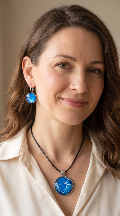 Frau trägt rundes Cabochon-Schmuckset mit Anhänger und Ohrringen an schwarzem Band, mit organischem Inselmuster in Kobaltblau, Azurblau, Cyan und hellen Linien.