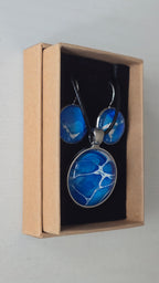 Rundes Cabochon-Schmuckset mit Anhänger und Ohrringen an schwarzem Band, mit organischem Inselmuster in Kobaltblau, Azurblau, Cyan und hellen Linien.