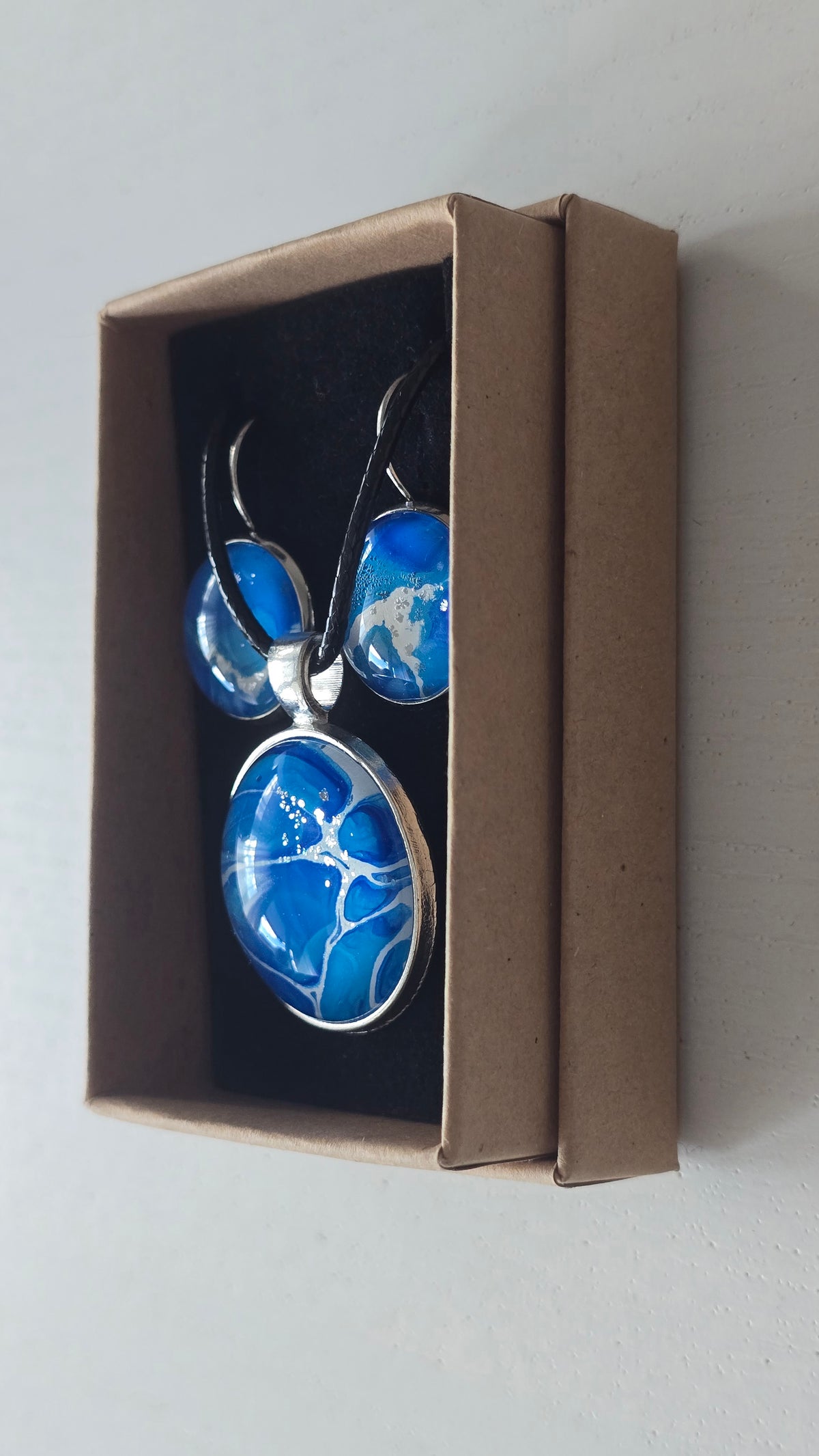 Rundes Cabochon-Schmuckset mit Anhänger und Ohrringen an schwarzem Band, mit organischem Inselmuster in Kobaltblau, Azurblau, Cyan und hellen Linien.